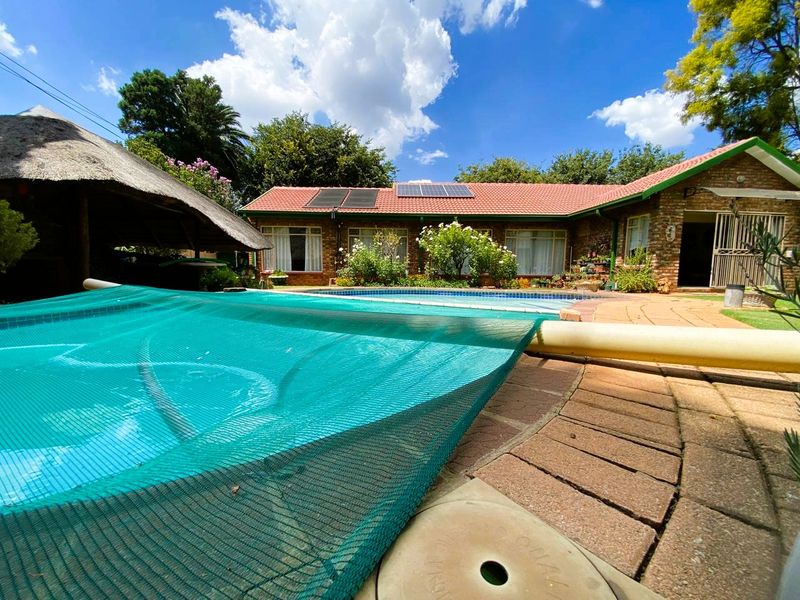 Outdoor pool area featuring a swimming pool with safety net, solar heating panels, brick paving, and an adjacent thatched lapa structure.