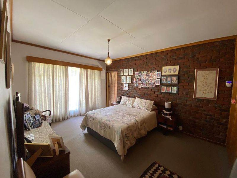 A bedroom featuring an exposed brick feature wall, carpeted flooring, and large windows with curtains, offering a classic and cozy atmosphere.