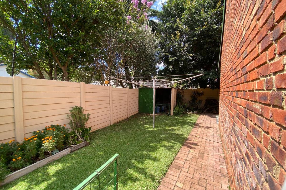 A private rear garden featuring a brick boundary wall, paved walkway, well-maintained lawn, and a small storage shed.