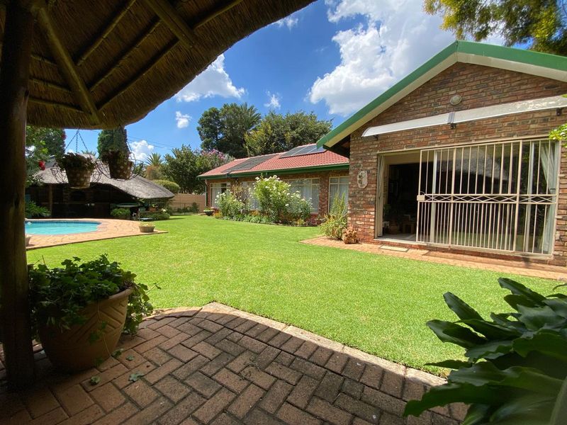 A well-maintained rear garden featuring a swimming pool, brick-built house with solar panels, and a covered patio area.
