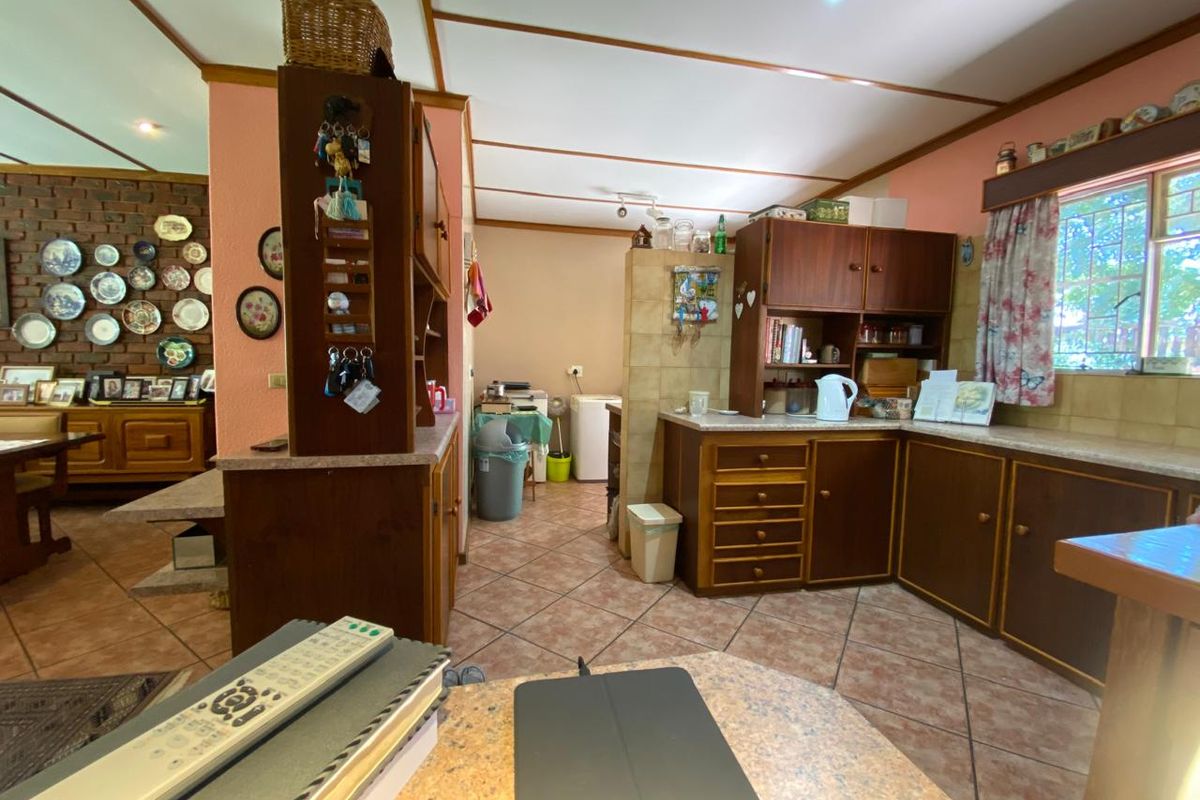 A functional kitchen featuring traditional wooden cabinetry, laminate countertops, and tiled flooring, with an adjacent dining area showcasing an exposed brick feature wall.