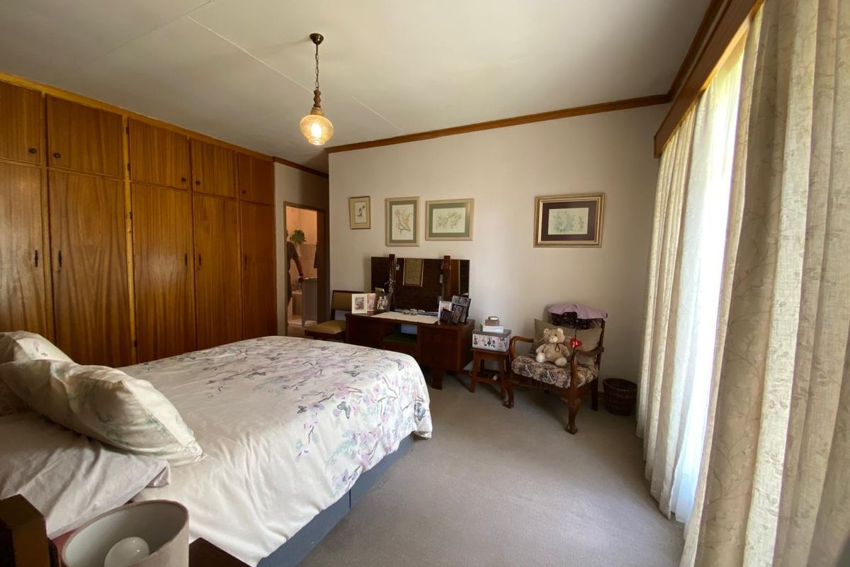 A spacious bedroom featuring extensive built-in wooden cabinetry, neutral carpeting, and large windows with natural light.