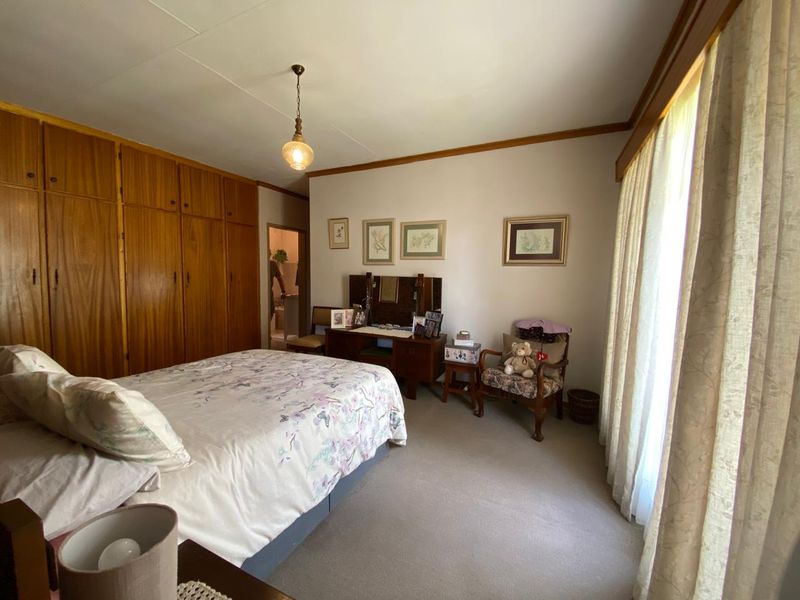 A spacious bedroom featuring extensive built-in wooden cabinetry, neutral carpeting, and large windows with natural light.