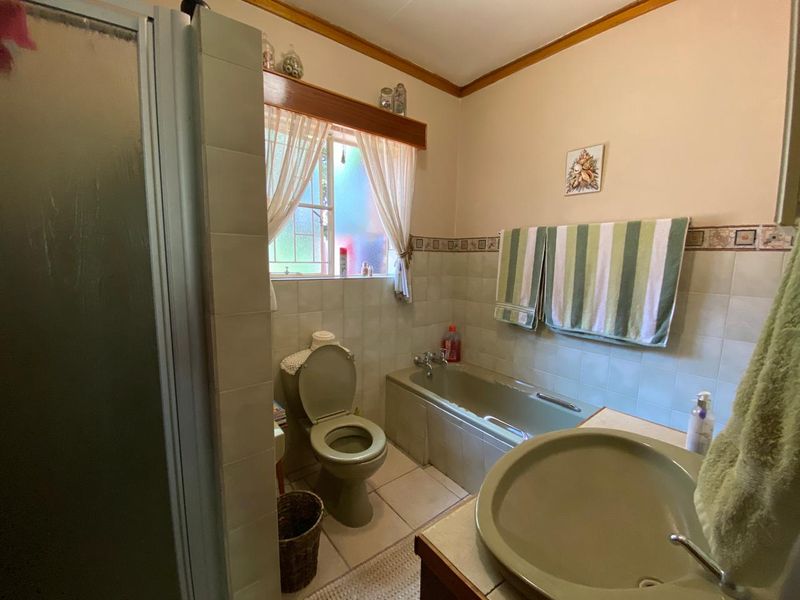 A dated bathroom featuring a bathtub, toilet, vanity basin, and separate shower enclosure with neutral wall and floor tiling.