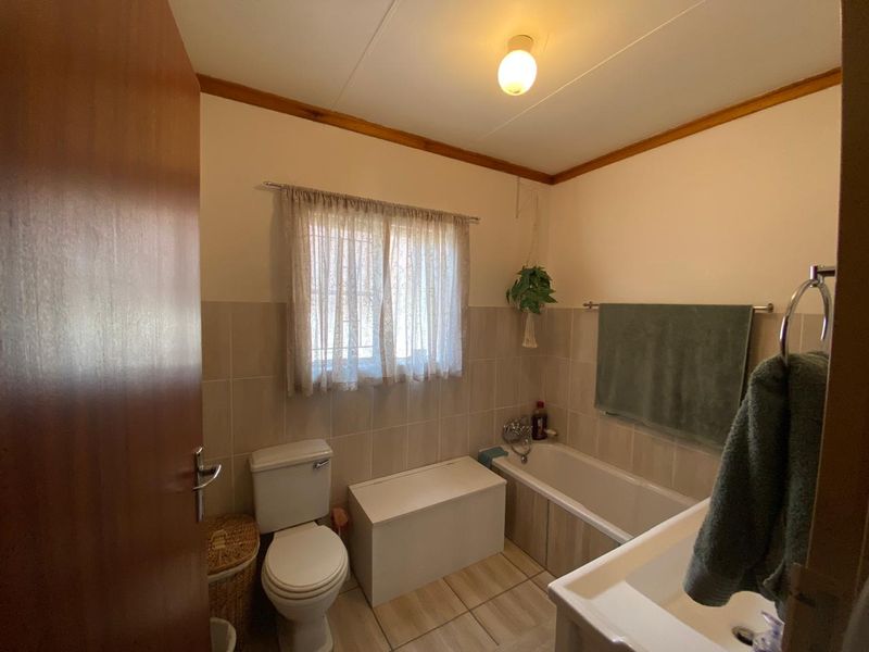 A functional bathroom featuring a bathtub, toilet, and neutral wall and floor tiling, offering a clean and practical space.