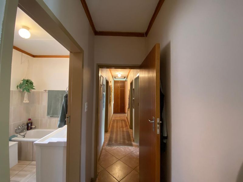 A view from the hallway looking towards a bathroom and a long corridor with built-in storage and tiled flooring.