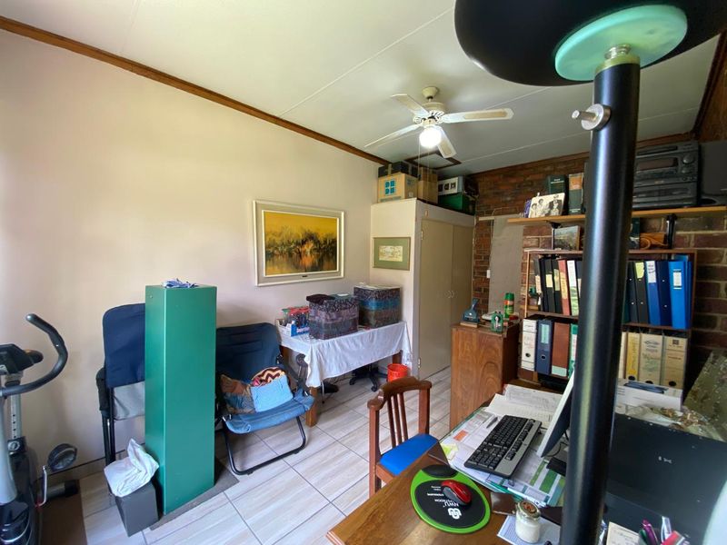 A functional home office space featuring tiled flooring, an exposed brick wall, a ceiling fan, and a built-in storage cupboard.