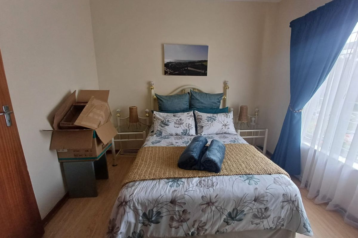 A well-lit bedroom featuring light wood-look flooring and a large window with blue curtains, providing a comfortable and functional living space.