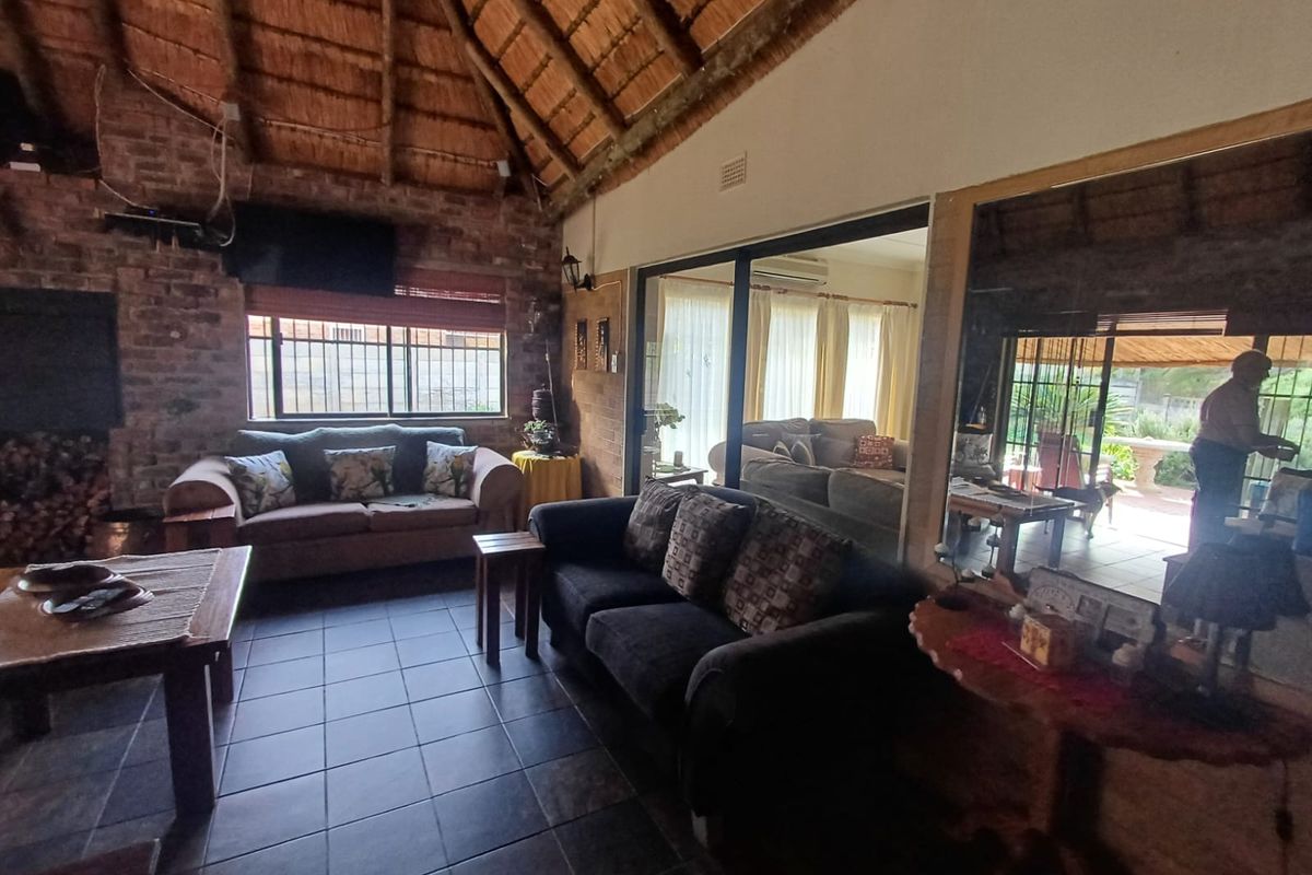 Spacious living area featuring a high vaulted thatch ceiling, exposed brick feature wall, tiled flooring, and large sliding glass doors leading to the patio.