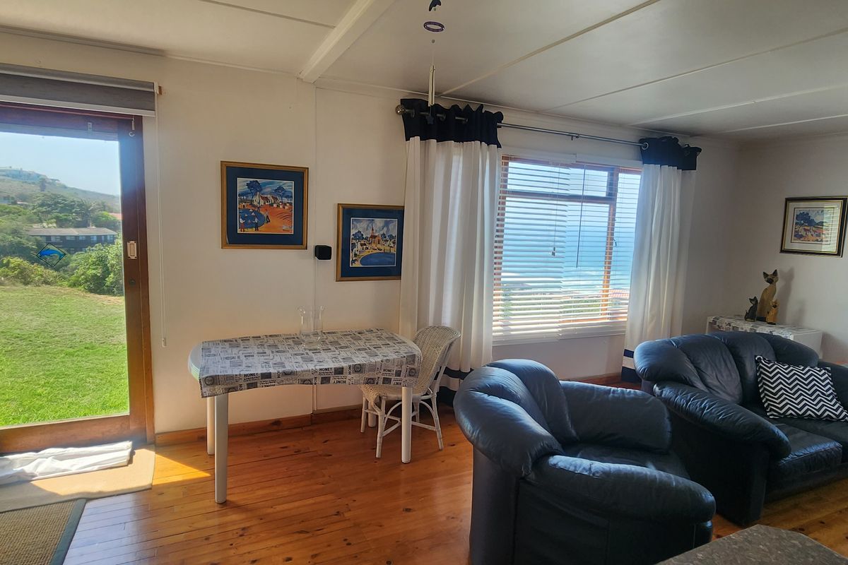 A bright living area featuring polished timber flooring, large windows with ocean views, and direct access to the garden through a glass door.