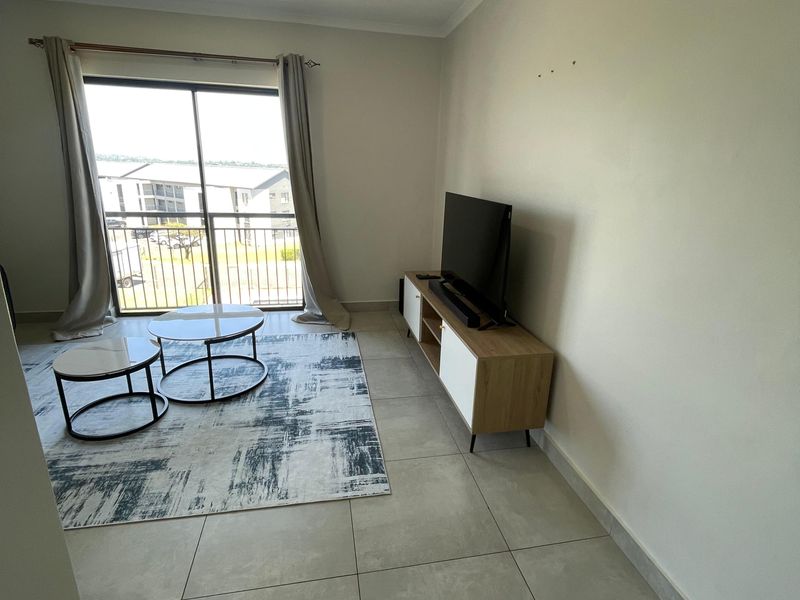 A bright living room featuring large sliding glass doors leading to a balcony, neutral tiled flooring, and recessed ceiling lighting.