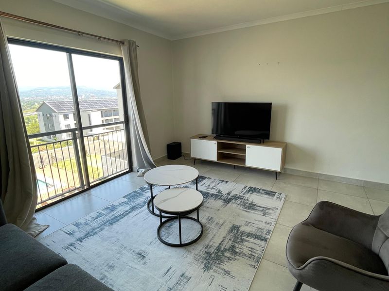 A bright living room featuring large sliding glass doors that open to a balcony, providing natural light and scenic views.