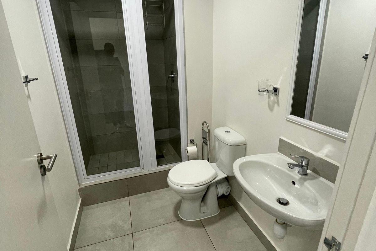 A clean and functional bathroom featuring a glass-enclosed shower, pedestal basin, wall-mounted mirror, and tiled flooring.