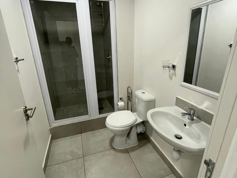 A clean and functional bathroom featuring a glass-enclosed shower, pedestal basin, wall-mounted mirror, and tiled flooring.
