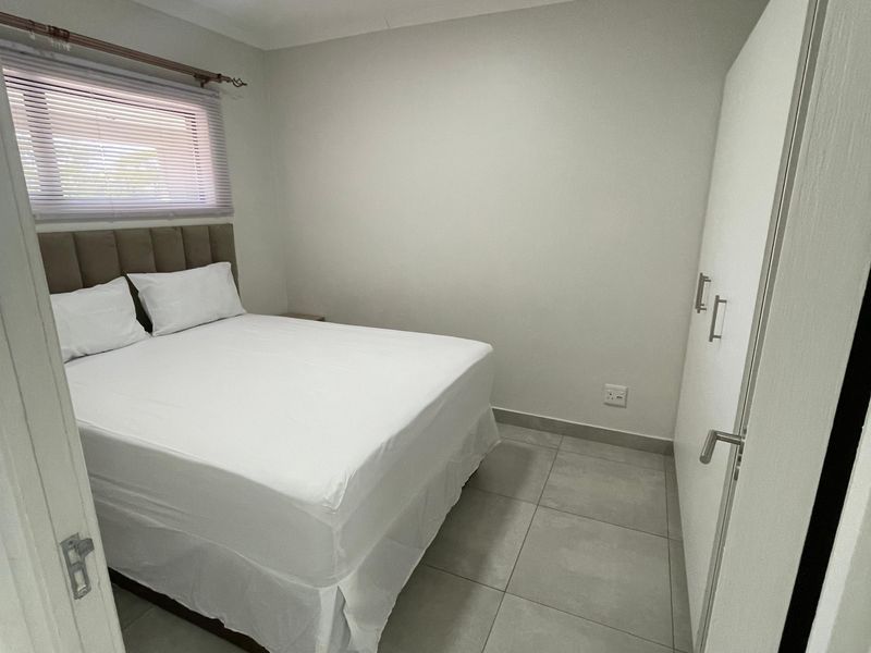 A clean and modern bedroom featuring neutral tiled flooring, built-in white cabinetry, and a window fitted with horizontal blinds.