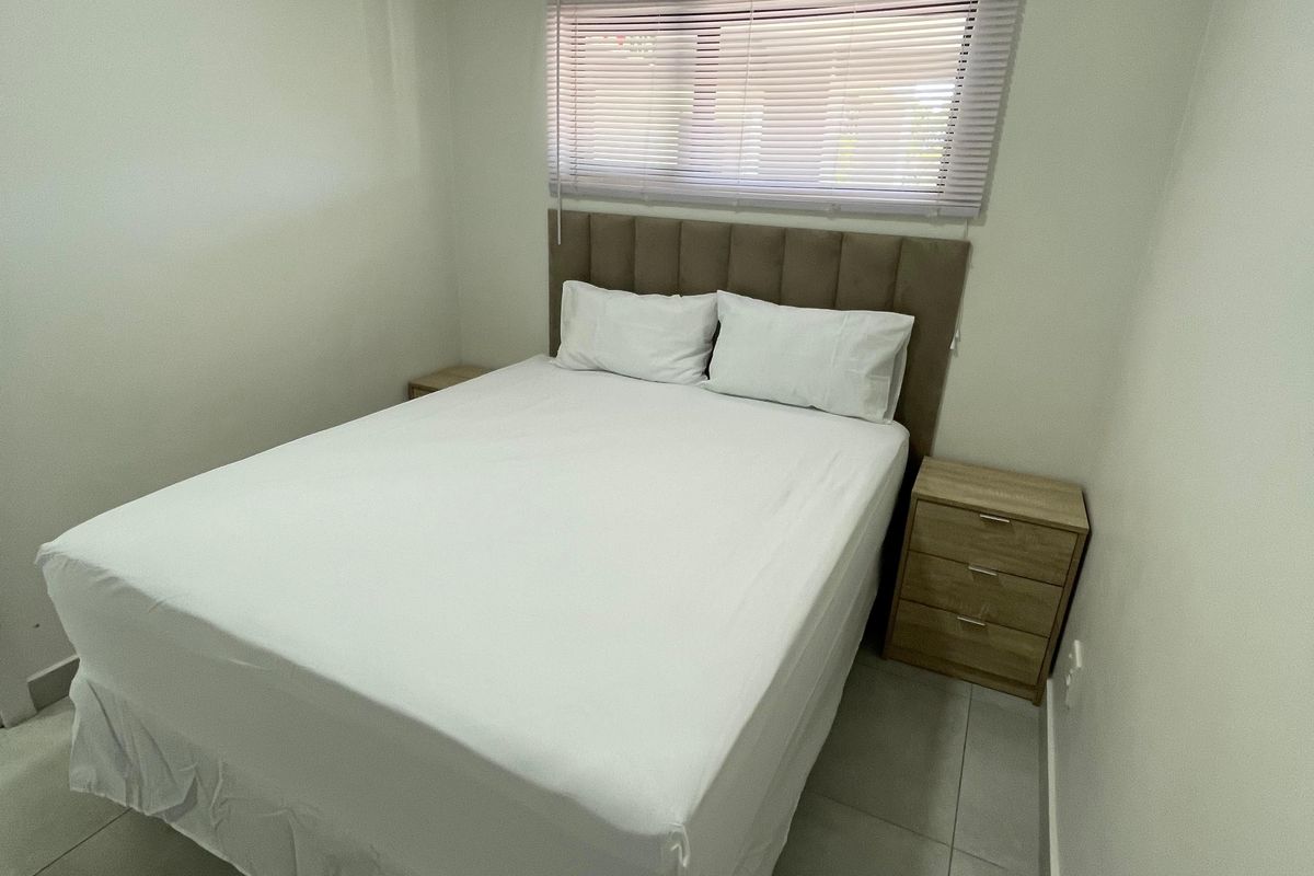 A clean and well-maintained bedroom featuring neutral tiled flooring, a window with fitted blinds, and a modern upholstered headboard.