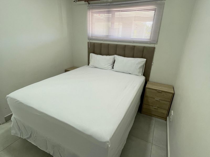 A clean and well-maintained bedroom featuring neutral tiled flooring, a window with fitted blinds, and a modern upholstered headboard.