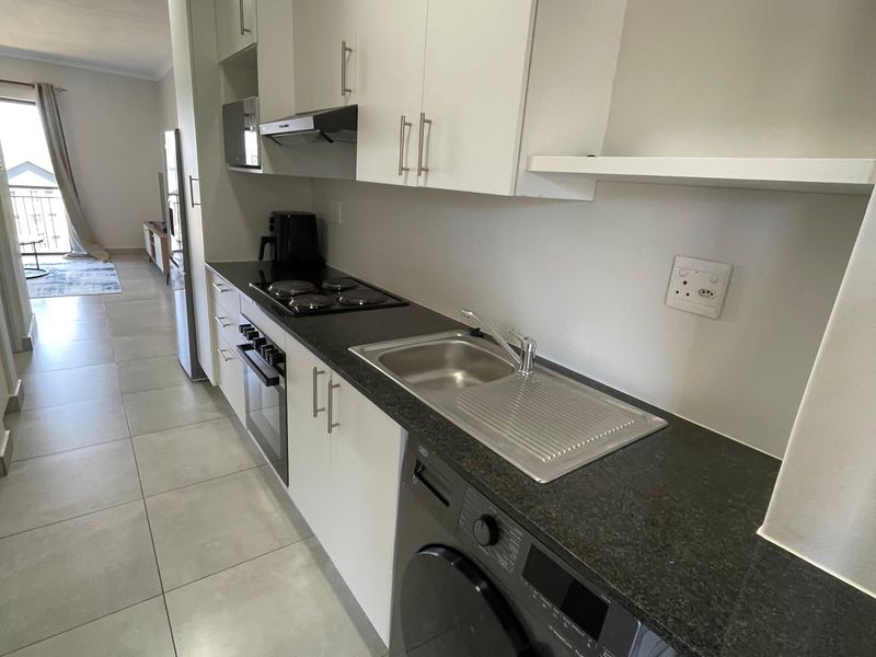 Modern galley-style kitchen featuring sleek white cabinetry, dark stone countertops, integrated hob, oven, extractor fan, and a dedicated space for laundry appliances.