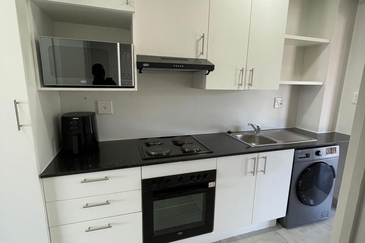 Modern kitchen featuring white cabinetry, black countertops, built-in oven, electric hob, extractor fan, and integrated space for a washing machine.