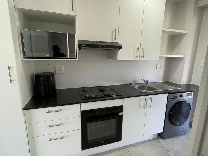 Modern kitchen featuring white cabinetry, black countertops, built-in oven, electric hob, extractor fan, and integrated space for a washing machine.