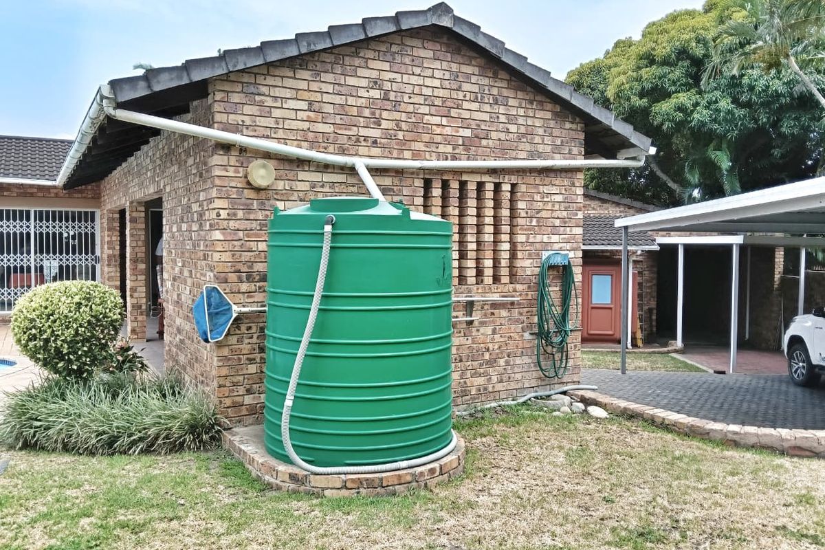 Rear exterior view of the property featuring a brick facade, tiled roof, and a large green water storage tank connected to the gutter system.