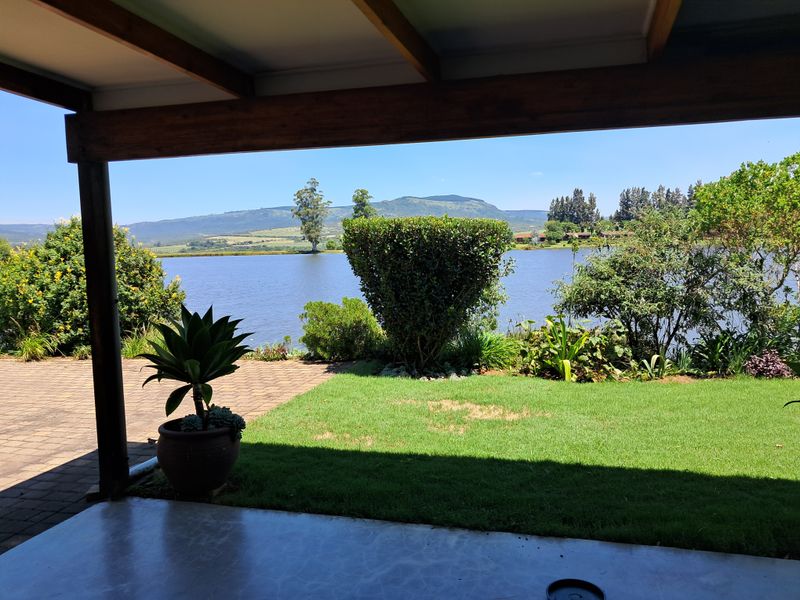 A covered patio area featuring timber beams and paved flooring, offering scenic views of the garden, lake, and surrounding mountains.