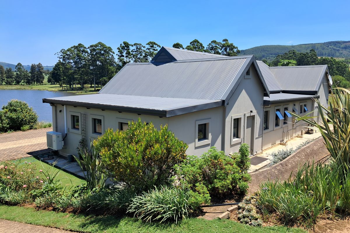 A well-maintained rear elevation of a house featuring a corrugated metal roof, landscaped garden, and scenic views of the adjacent lake.