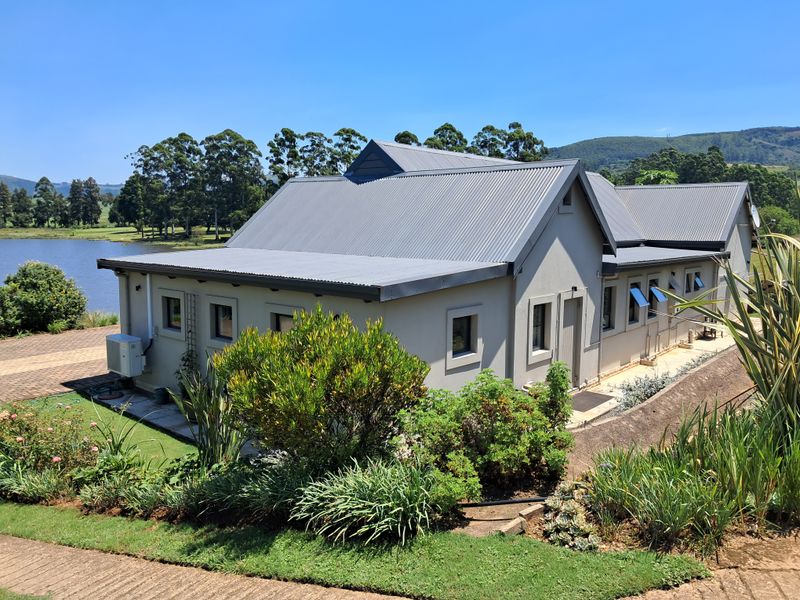 A well-maintained rear elevation of a house featuring a corrugated metal roof, landscaped garden, and scenic views of the adjacent lake.