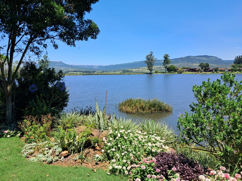 Scenic view overlooking a tranquil lake with lush landscaped garden foreground and distant mountain landscape.