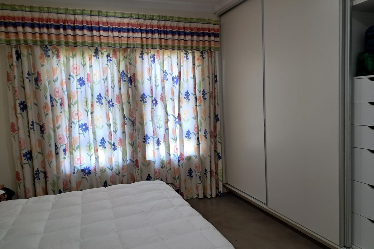 A bedroom featuring a large built-in sliding door wardrobe with integrated drawer storage and a window with decorative curtains.