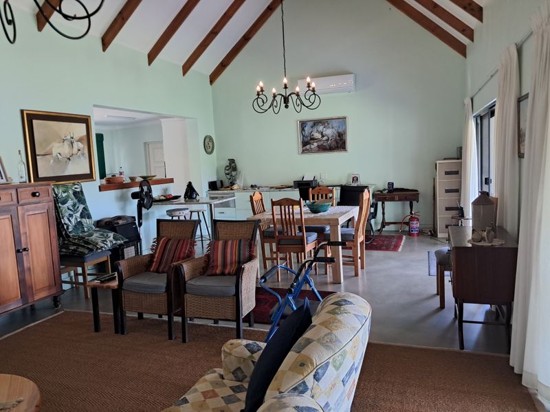 Spacious open-plan living and dining area featuring vaulted ceilings with exposed timber beams, concrete flooring, and a split-system air conditioner.