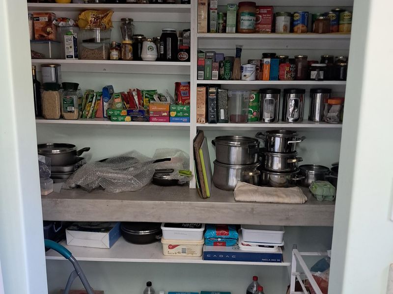 A functional walk-in pantry or scullery featuring extensive built-in shelving and a solid concrete countertop for additional storage and preparation space.