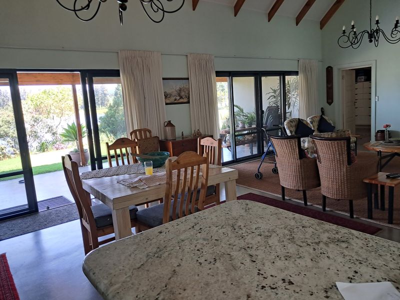 Spacious open-plan living and dining area featuring vaulted ceilings with exposed timber beams, granite kitchen island, and large sliding doors opening to the patio.