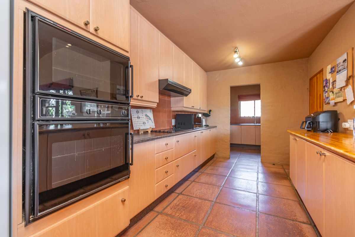 A functional kitchen featuring light wood cabinetry, built-in double ovens, tiled flooring, and a separate scullery area visible through the doorway.