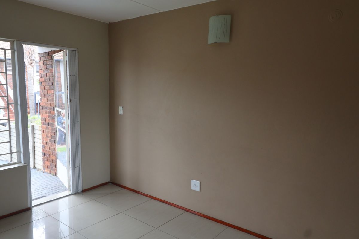 A bright, empty living area featuring tiled flooring, a wall-mounted light fixture, and a glass door providing direct access to the exterior.