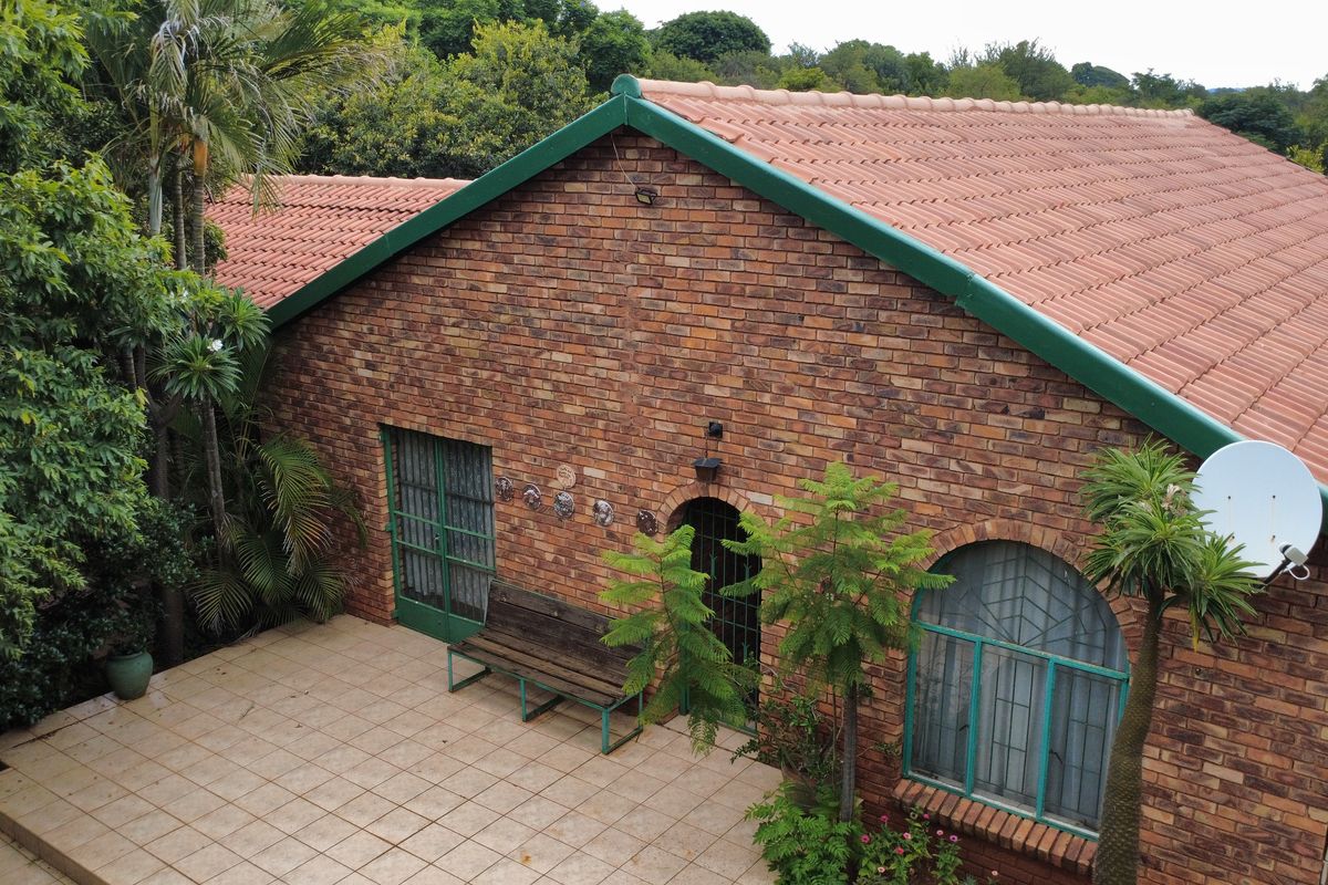 Rear view of a face brick home featuring a tiled patio, arched windows, and a pitched tiled roof set within a lush garden.