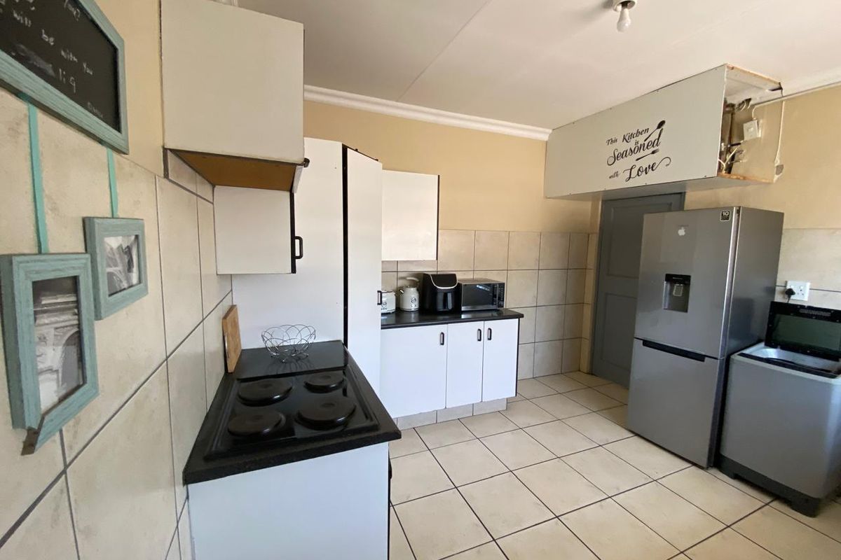 A functional kitchen featuring tiled flooring, a tiled backsplash, and built-in cabinetry, currently requiring repairs to the extractor fan housing and cabinetry finishes.