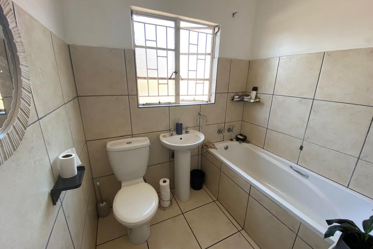 A functional bathroom featuring a pedestal basin, toilet, and bathtub with neutral wall and floor tiling.