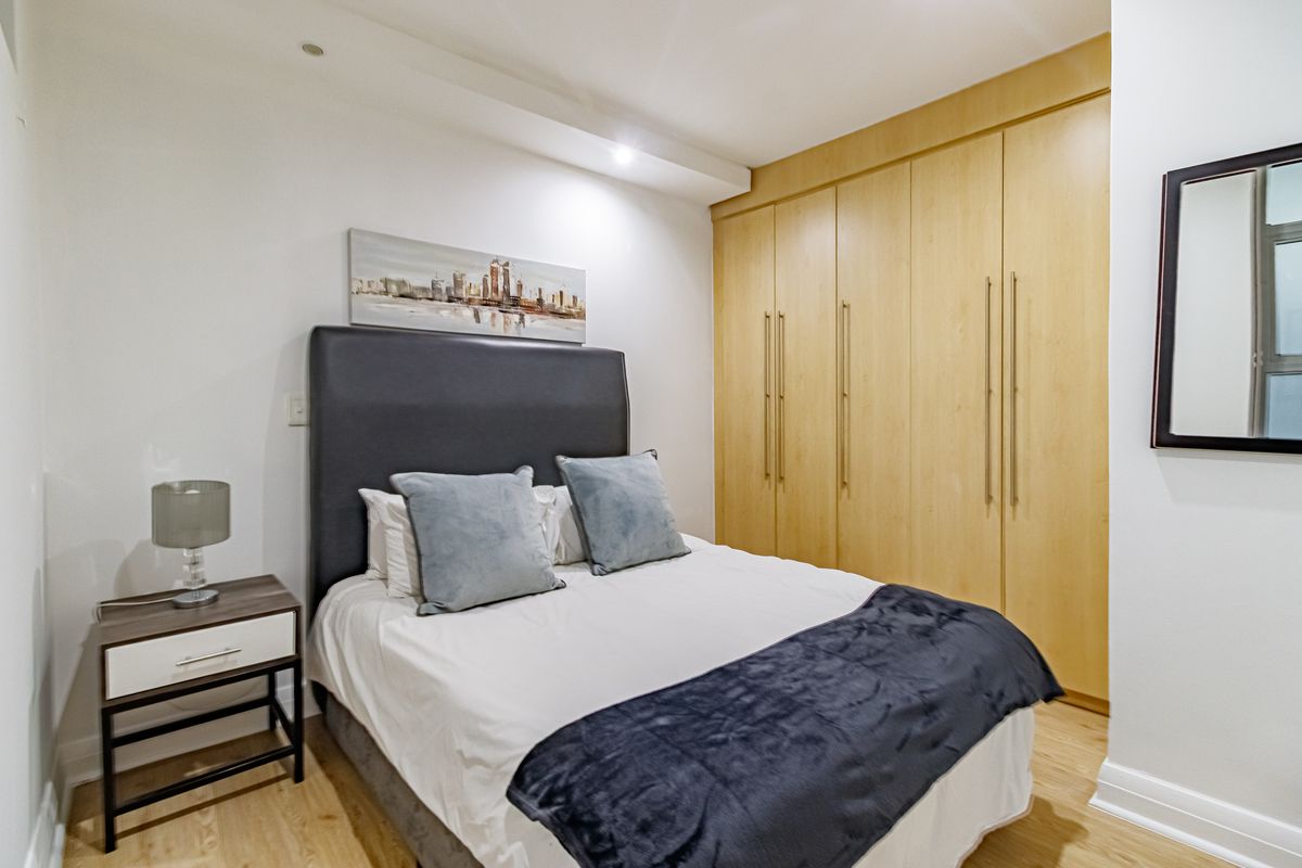 A well-maintained bedroom featuring light wood-finish built-in cupboards, recessed ceiling lighting, and neutral wall finishes.