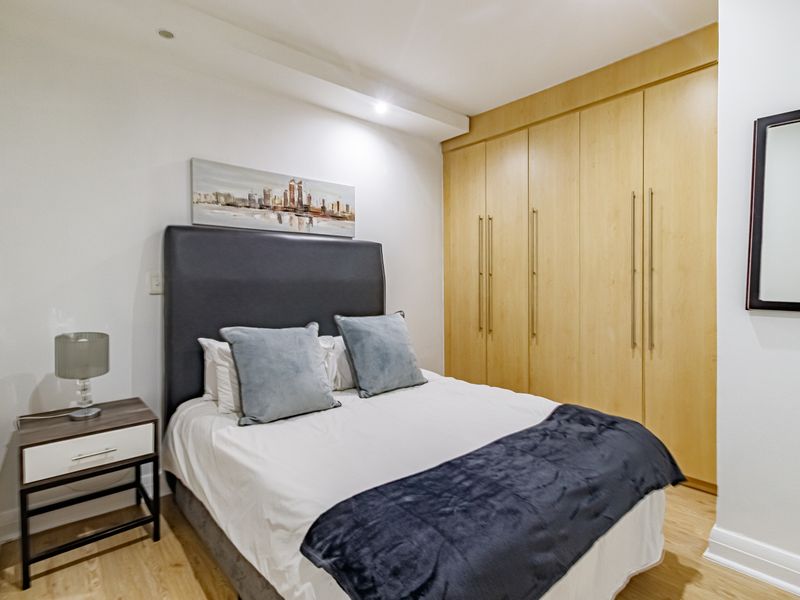 A well-maintained bedroom featuring light wood-finish built-in cupboards, recessed ceiling lighting, and neutral wall finishes.