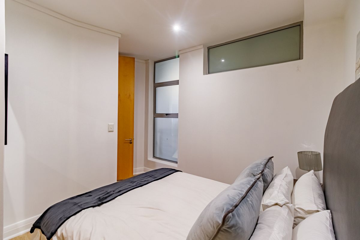 A modern bedroom featuring neutral walls, recessed downlighting, and frosted glass windows providing natural light while maintaining privacy.