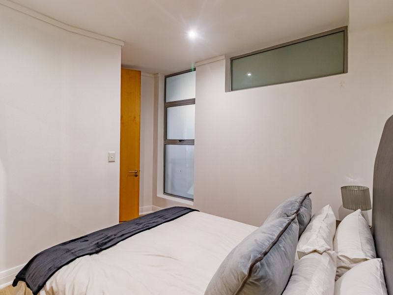 A modern bedroom featuring neutral walls, recessed downlighting, and frosted glass windows providing natural light while maintaining privacy.