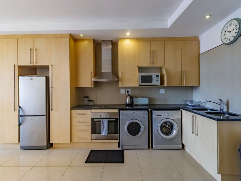 A functional kitchen featuring light wood cabinetry, stainless steel appliances, built-in oven and hob, and tiled flooring with integrated laundry space.