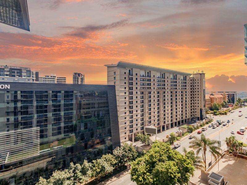 An elevated urban view showcasing the surrounding city skyline, modern commercial buildings, and street-level infrastructure during a vibrant sunset.