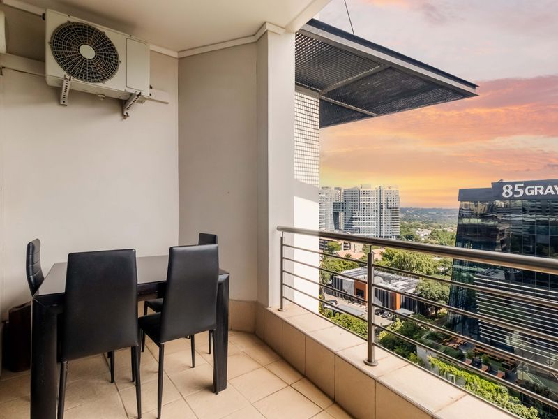 A covered balcony featuring tiled flooring, a stainless steel balustrade, and an installed air conditioning unit, offering elevated urban views.