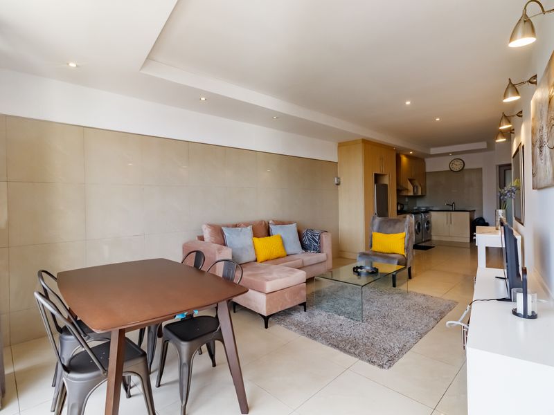 An open-plan living and kitchen area featuring tiled flooring, recessed ceiling lighting, and a modern tiled feature wall, creating a cohesive and functional space.
