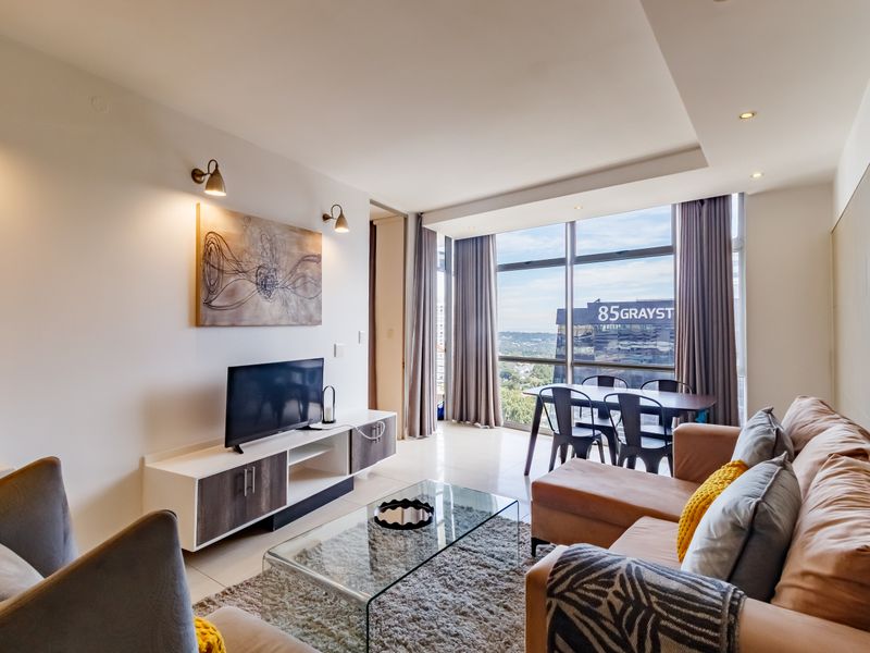 A bright open-plan living and dining area featuring floor-to-ceiling windows with city views, recessed ceiling lighting, and modern tiled flooring.