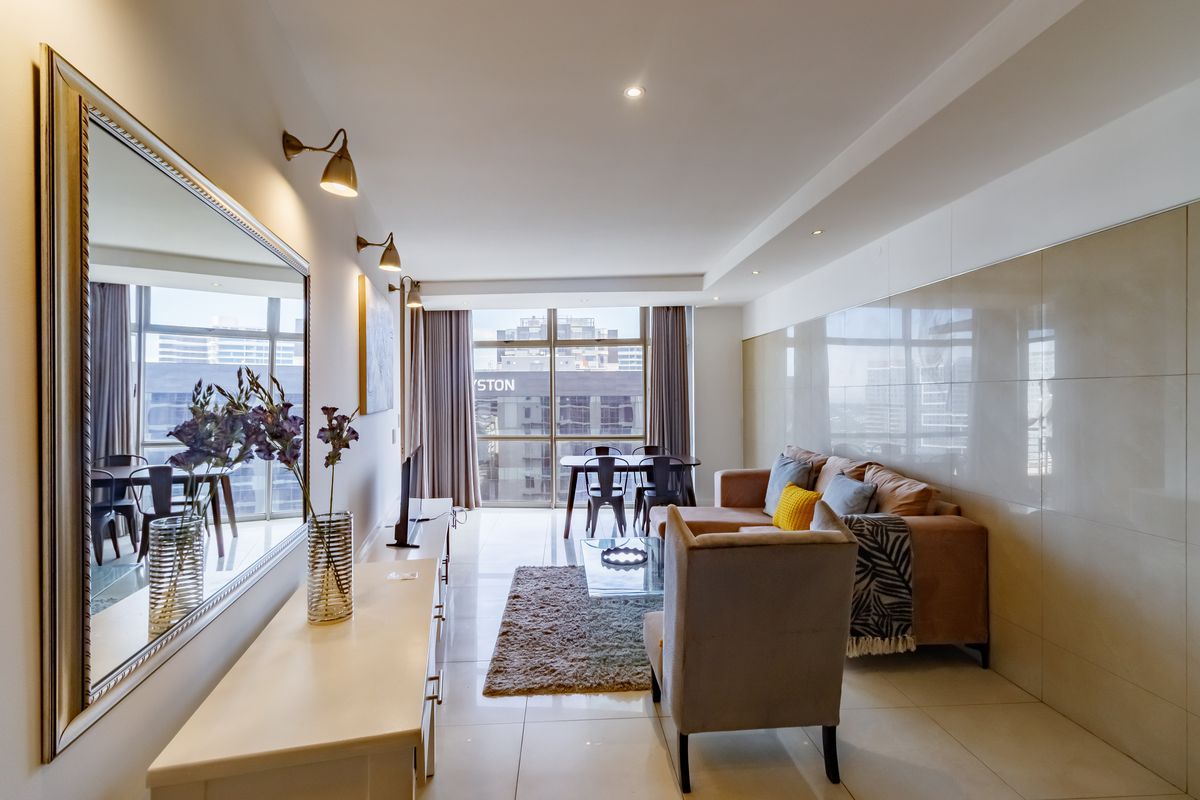 Modern open-plan living and dining area featuring large format wall tiles, recessed lighting, and floor-to-ceiling windows with urban views.