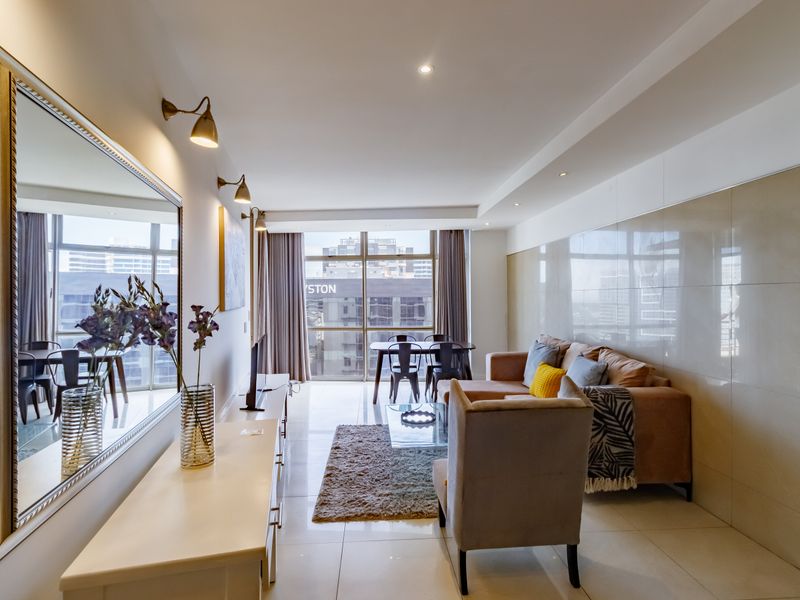 Modern open-plan living and dining area featuring large format wall tiles, recessed lighting, and floor-to-ceiling windows with urban views.