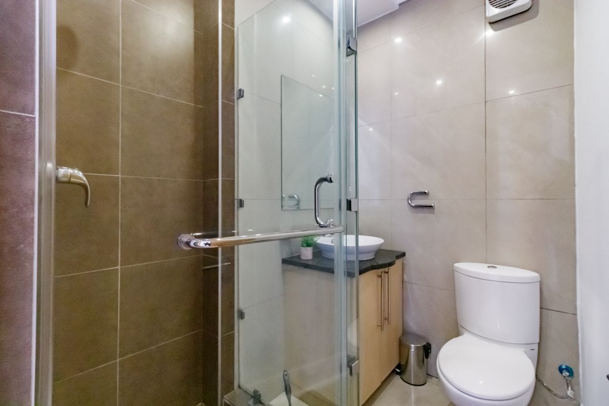 Modern bathroom featuring a glass-enclosed shower, vanity cabinet with vessel sink, and a standard toilet with neutral wall tiling.